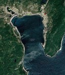 Google map of a coastal harbour showing terrain and green vegetation surrounding the water on three sides.